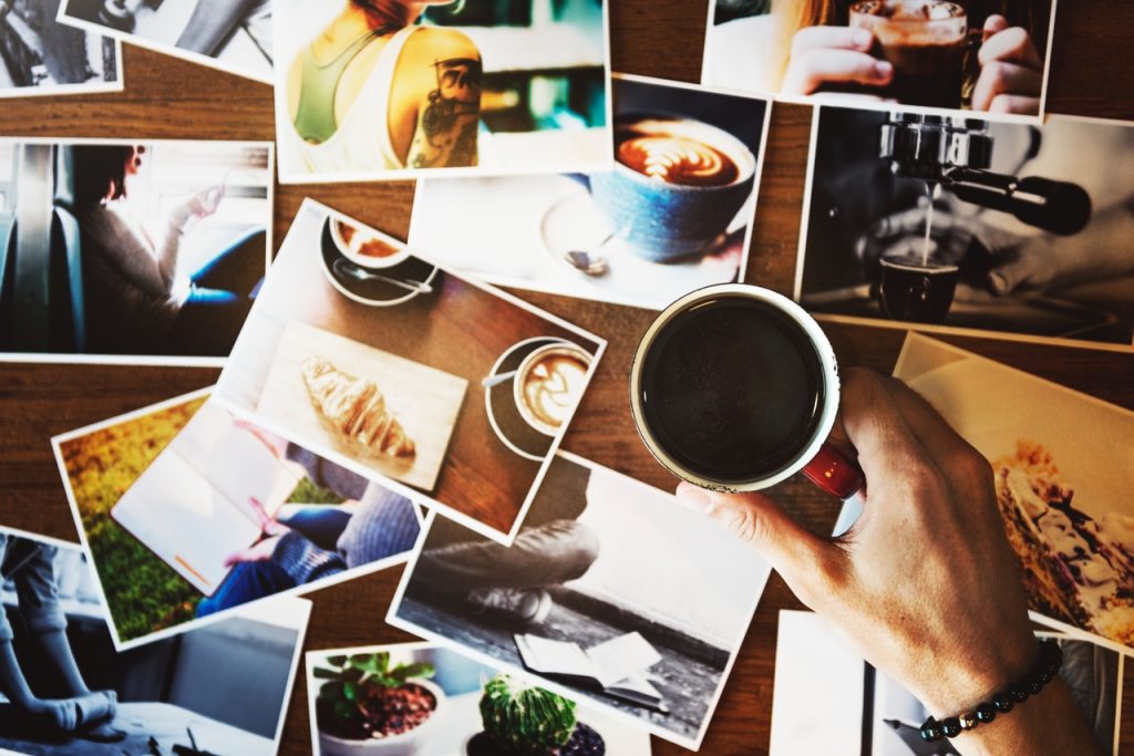 top view of person holding printed coffee on top of printed photos scattered on wooden surface