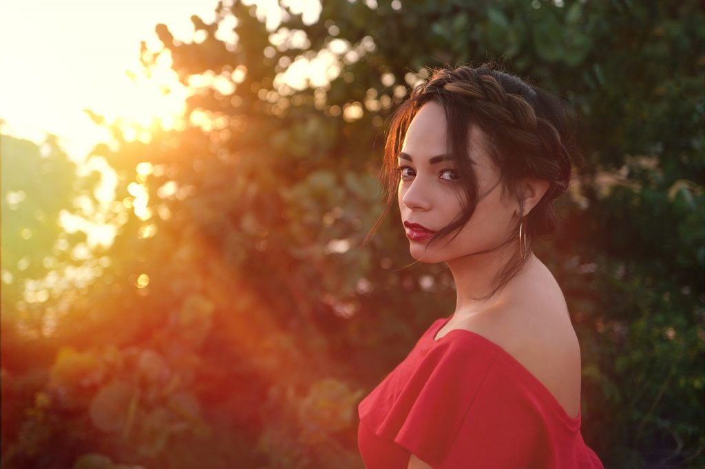 woman wearing red backless shirt and red lipstick standing beside trees at sunset